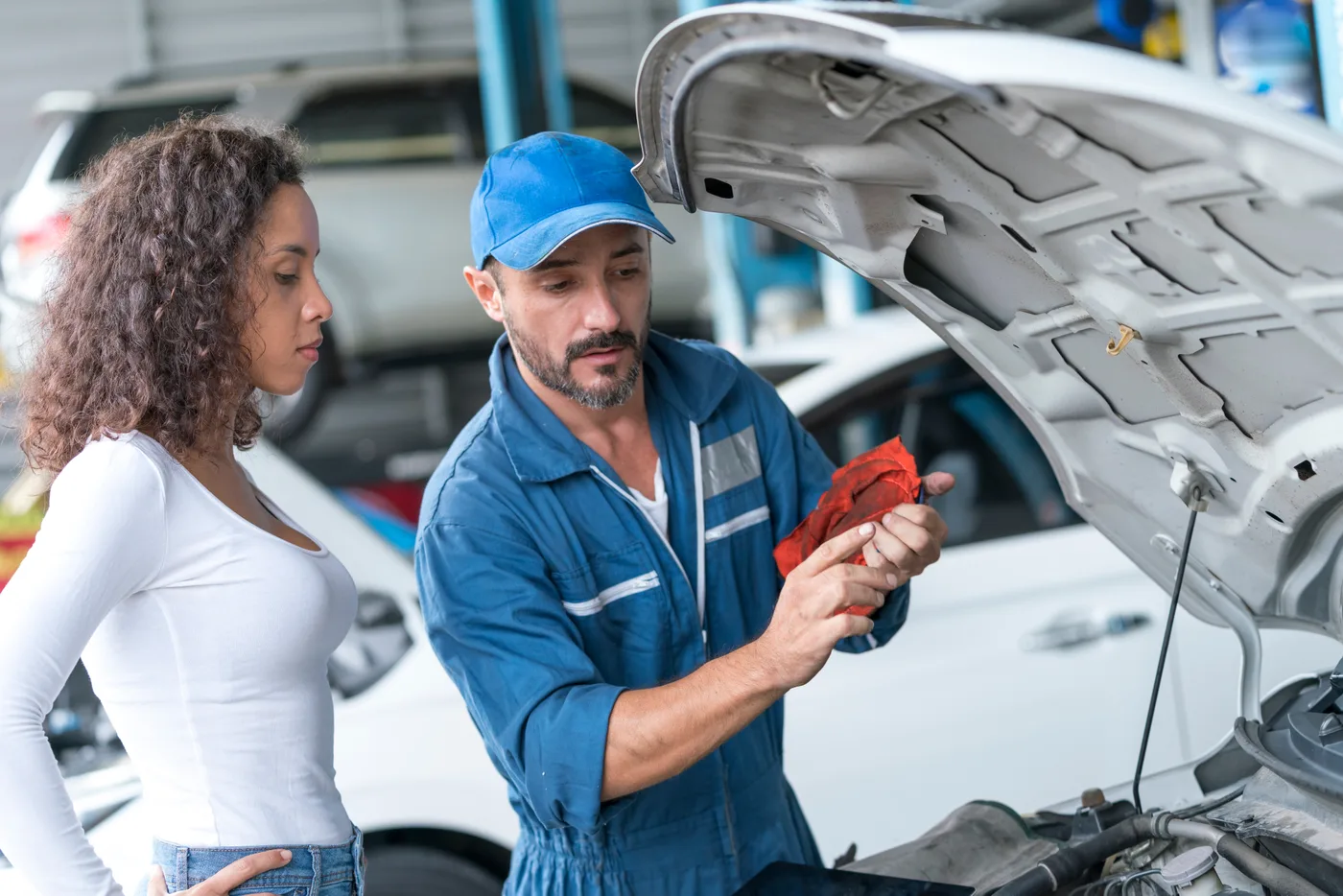 Mechaniker erklärt einer Kundin etwas am geöffneten Motorraum